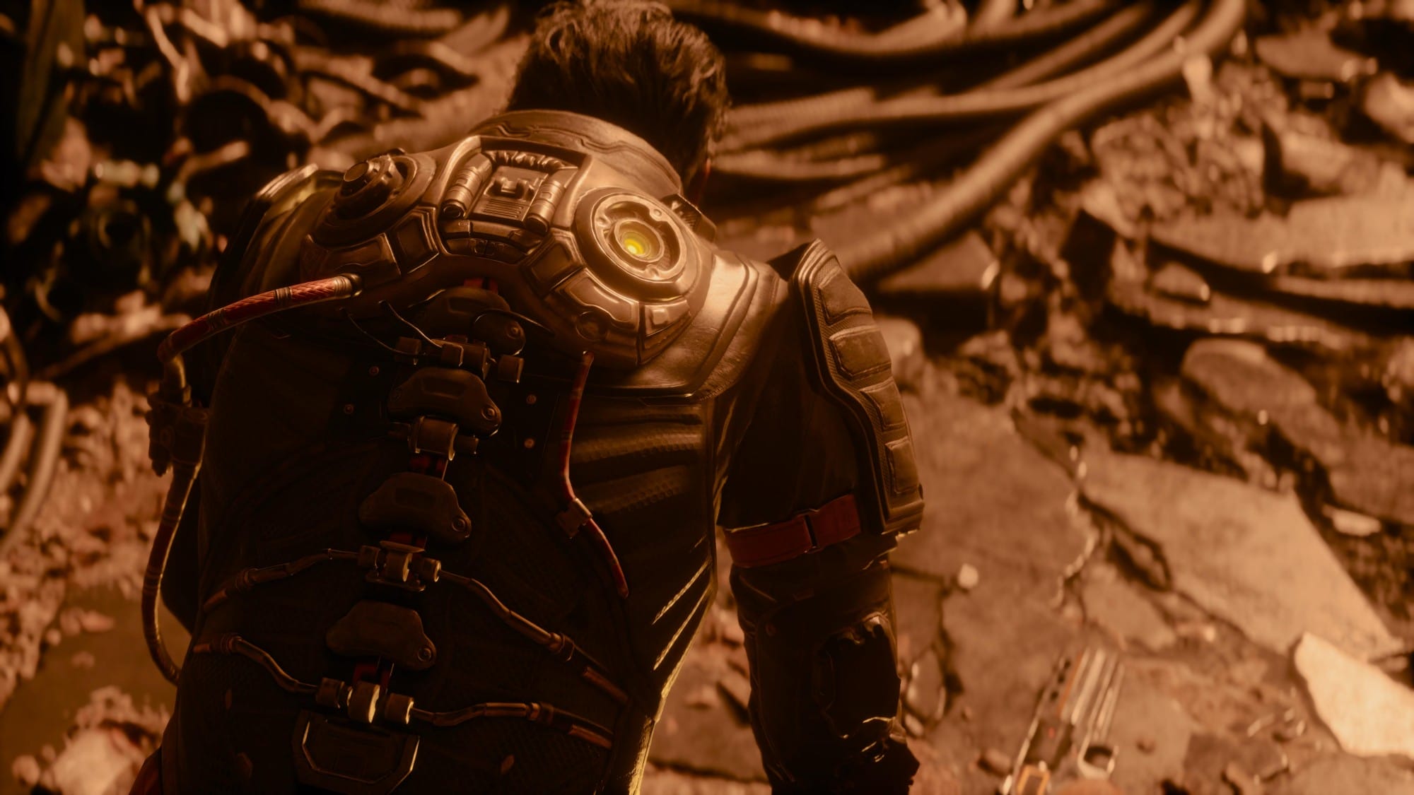 Back view of a person wearing a high-tech armored exosuit with cables and a glowing circular unit on the shoulder, in a rocky outdoor setting