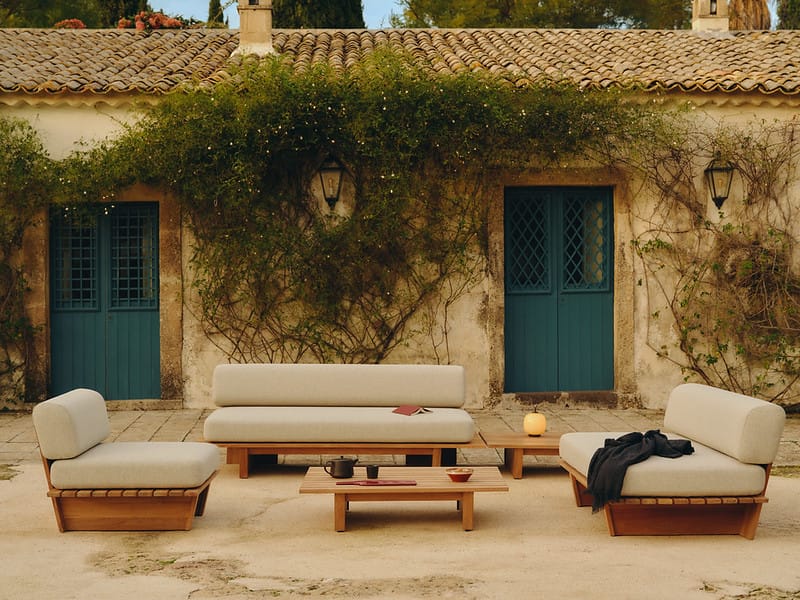 Outdoor lounge set with beige cushions and low wooden table on a stone patio in an ivy-covered courtyard.