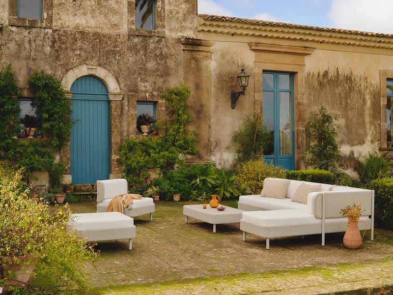 Stone villa courtyard with blue doors, potted plants, and white outdoor sectional seating on a stone-paved patio.